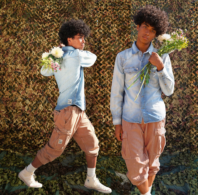 Young Man holding flowers wearing a long sleeve medium blue denim shirt and vintage washed adobe brown cargo pant 